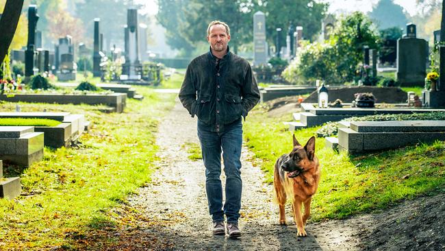 Chefinspektor Max Steiner geht an einem sonnigen Tag mit Polizeihund Rex einem Weg durch die Gräberzeilen eines Friedhofs entlang