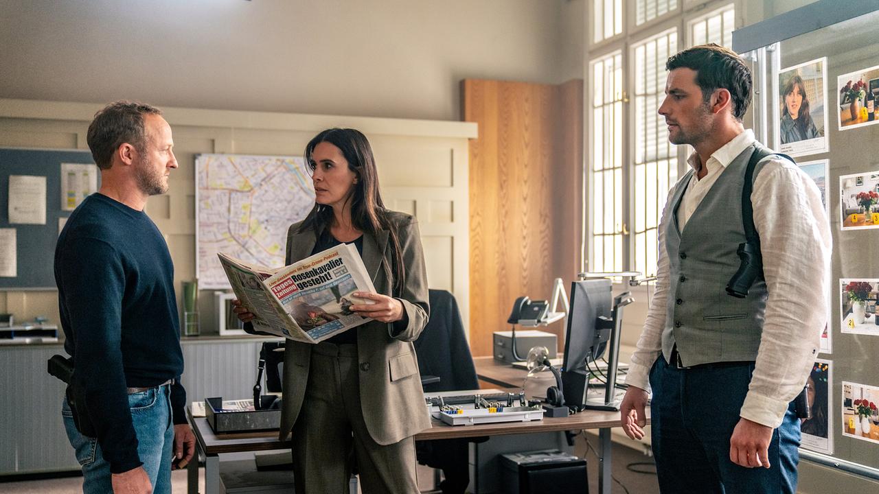 Im Büro der Kriminalpolizei, Majorin Evelyn Leitner hält eine Tageszeitung mit der Schlagzeile 'Rosenkavalier gesteht!' in den Händen und unterhält sich mit Max und Felix 