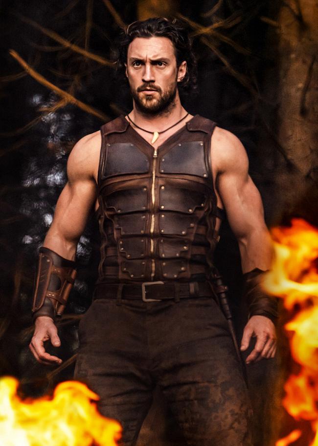 Aaron Taylor-Johnson als Kraven im Lederharnisch, kampfbereit steht er in einem Wald, vor ihm lodert ein Feuer