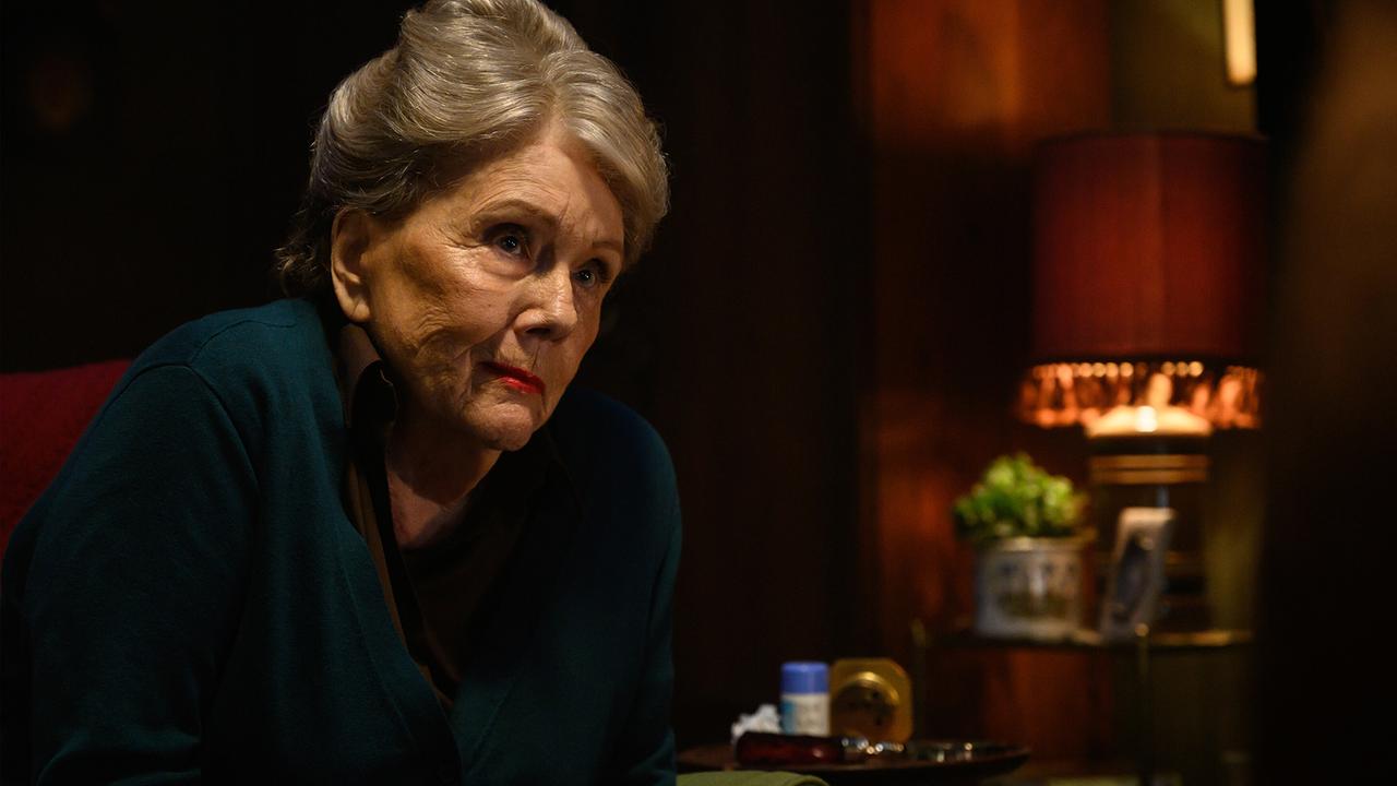 © ORF/Universal Pictures Eine weißhaarige Frau sitzt in einem dunklen Raum an einem Tisch und blickt nach oben, hinter ihr eine stilvolle Lampe