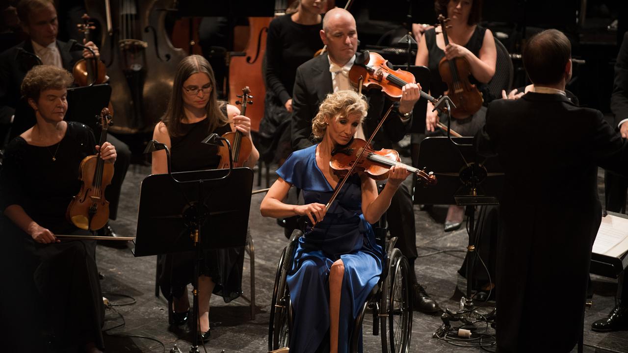 © ORF/SilkWayFilms/NFP/Gaumont/La Boétie Films/Pour Toi Public Prod./TF1 Films Production/Nicolas Schul Bei einem Konzert spielt Florence die erste Geige, in einem blauen Kleid sitzt sie in einem Rollstuhl
