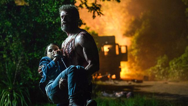 © ORF/© 2017 Marvel. TM and © 2017 Twentieth Century Fox Film/Ben Rothstein Hugh Jackman als Wolverine trägt Dafne Keen als das Mädchen Laura Kinney, auf der Sraße, die durch ein Waldstück führt, brennt im Hintergrund ein Lieferwagen