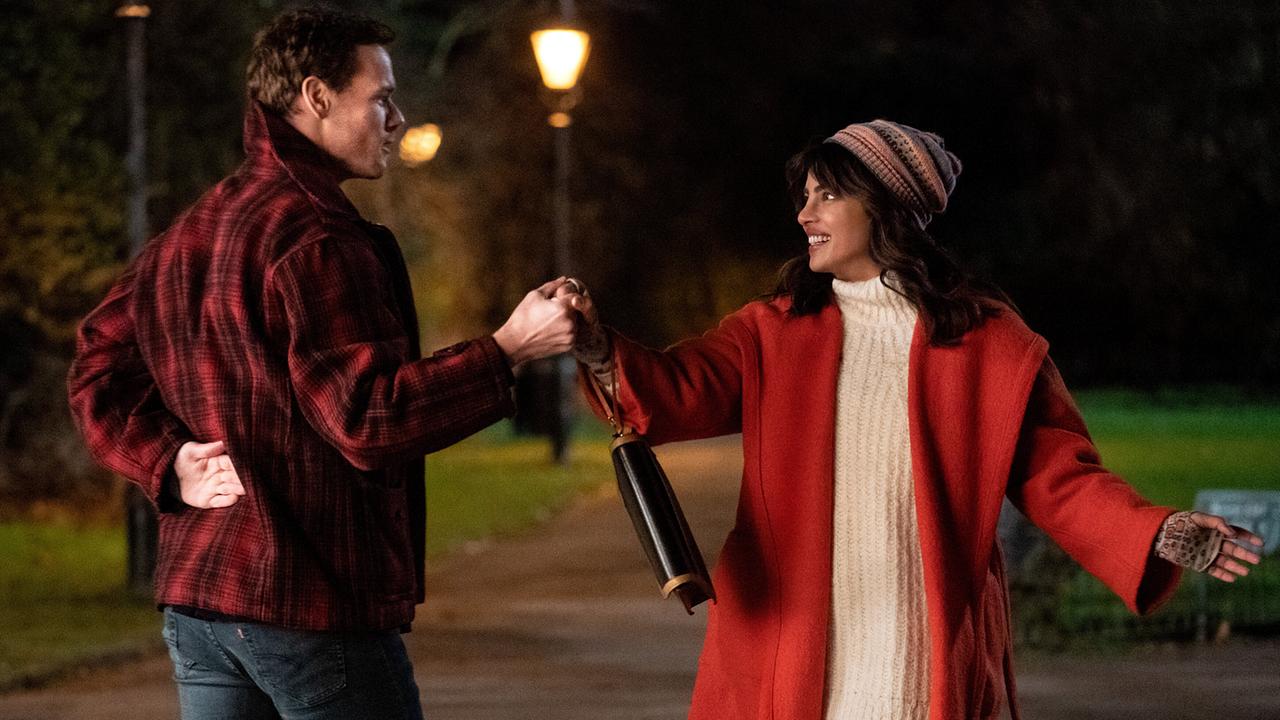 Ein Mann in rot-schwarz-karierter Jacke und eine Frau in weißem Pulli, roter Jacke und Haube tanzen in der Nacht in einem Park