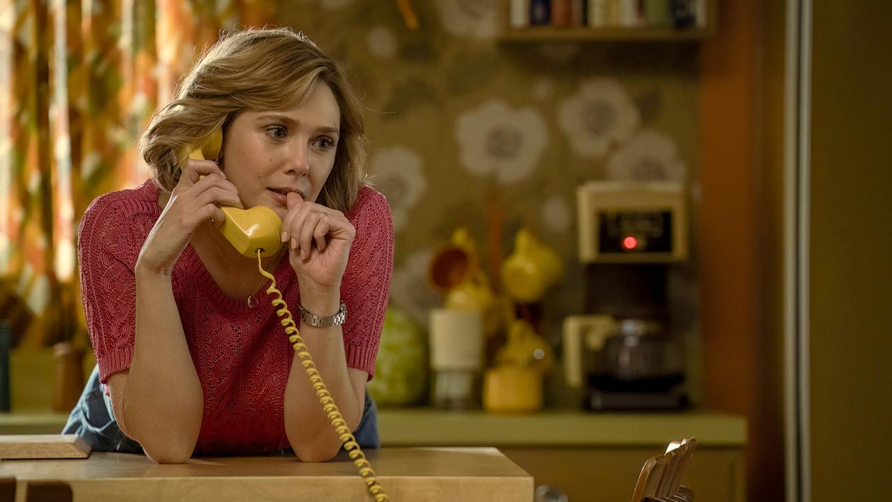 © ORF/Warner/HBO Max Elizabeth Olsen als Candy Montgomery telefoniert mit einem gelben Festnetztelefon in einer Küche mit bunt gemusterten Vorhängen und Tapeten, verträumt blickt sie bei dem Gespräch ins Leere und hält den Daumennagel an ihre Lippen