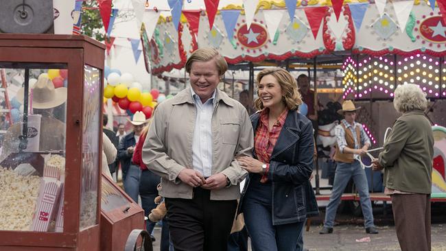 Jesse Plemons als Allan Gore und Elizabeth Olsen als Candy Montgomery gehen vergnügt bei einem Jahrmarkt bei einem Ringelspiel und einem Popcorn-Stand vorbei