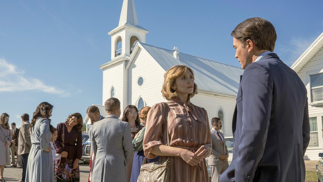 Elizabeth Olsen als Candy Montgomery, am Vorplatz eines kleinen, weißen Kirchengebäudes unterhält sie sich mit Tom Pelphrey als Don Crowder, hinter ihnen weitere Mitglieder der Krichengemeinde