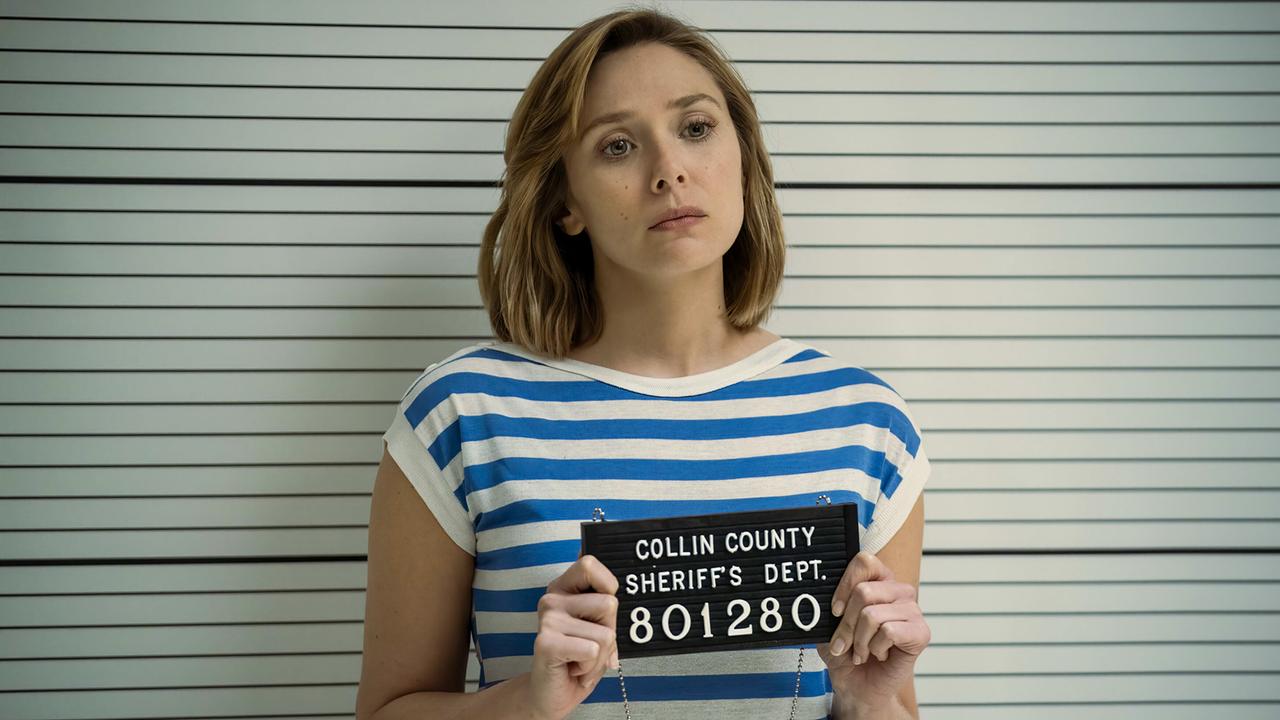 © ORF/Warner/HBO Max Elizabeth Olsen als Candy Montgomery steht sie bei der Verhaftung in einem blau-weißen Shirt vor einer Wand mit waagerechten Linien, in den Händen hält sie ein Schild mit der Aufschrift 'Collin County Sheriffs Dept. 801280'