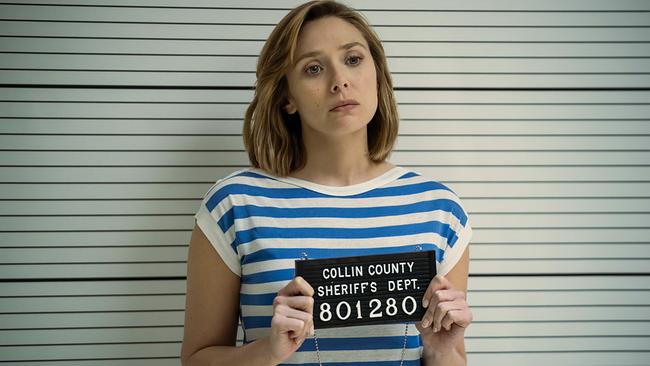 Elizabeth Olsen als Candy Montgomery steht sie bei der Verhaftung in einem blau-weißen Shirt vor einer Wand mit waagerechten Linien, in den Händen hält sie ein Schild mit der Aufschrift 'Collin County Sheriffs Dept. 801280'