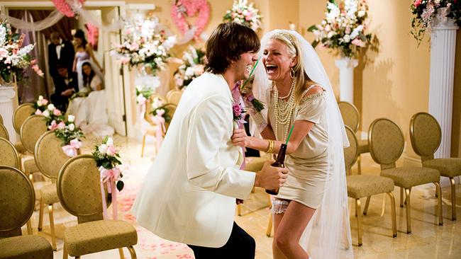 © ORF/New Regency/20th Century Studios/K.C. Bailey Eine Frau und ein Mann sind feierlich in weiß gekleidet halten Bierflaschen mit Strohhalmen in der Hand, in dem festlich geschmückten Raum krümmen sie sich vor Lachen