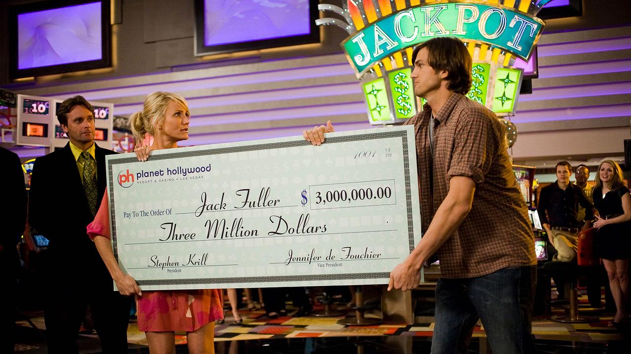 © ORF/New Regency/20th Century Studios/K.C. Bailey Eine Frau und ein Mann halten auf einer Bühne einen Scheck über 3 Millionen Dollar in den Händen, sie blicken sich dabei ernst in die Augen, im Hintergrund ist der Schriftzug Jackpot zu lesen