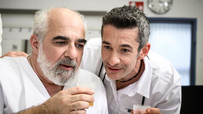 Michael Niavarani und Omar Sarsam in weißen Arztkitteln begutachten in einer Praxis konzentriert eine Urinprobe.