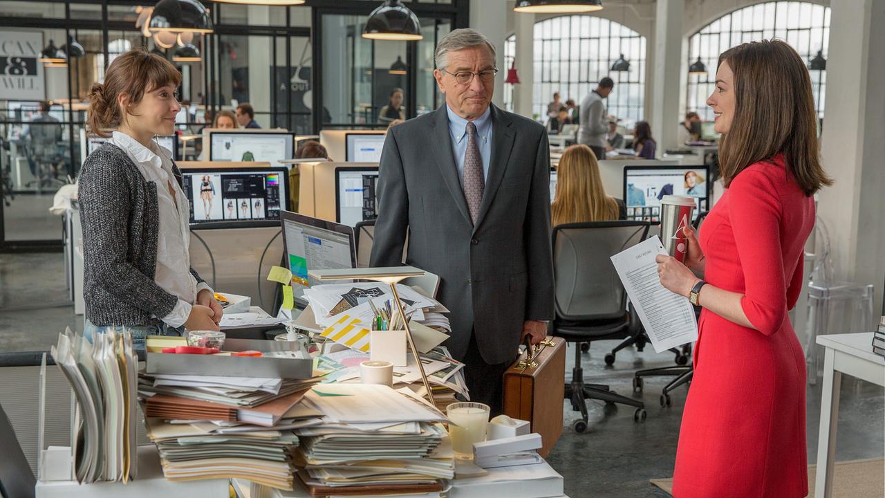 © ORF/Warner Bros. Pictures Eine Frau in weißer Bluse und grauer Strickjacke, ein Mann in Business-Anzug und eine Frau in einem roten Kleid stehen um einen Schreibtisch, auf dem sich die Akten türmen