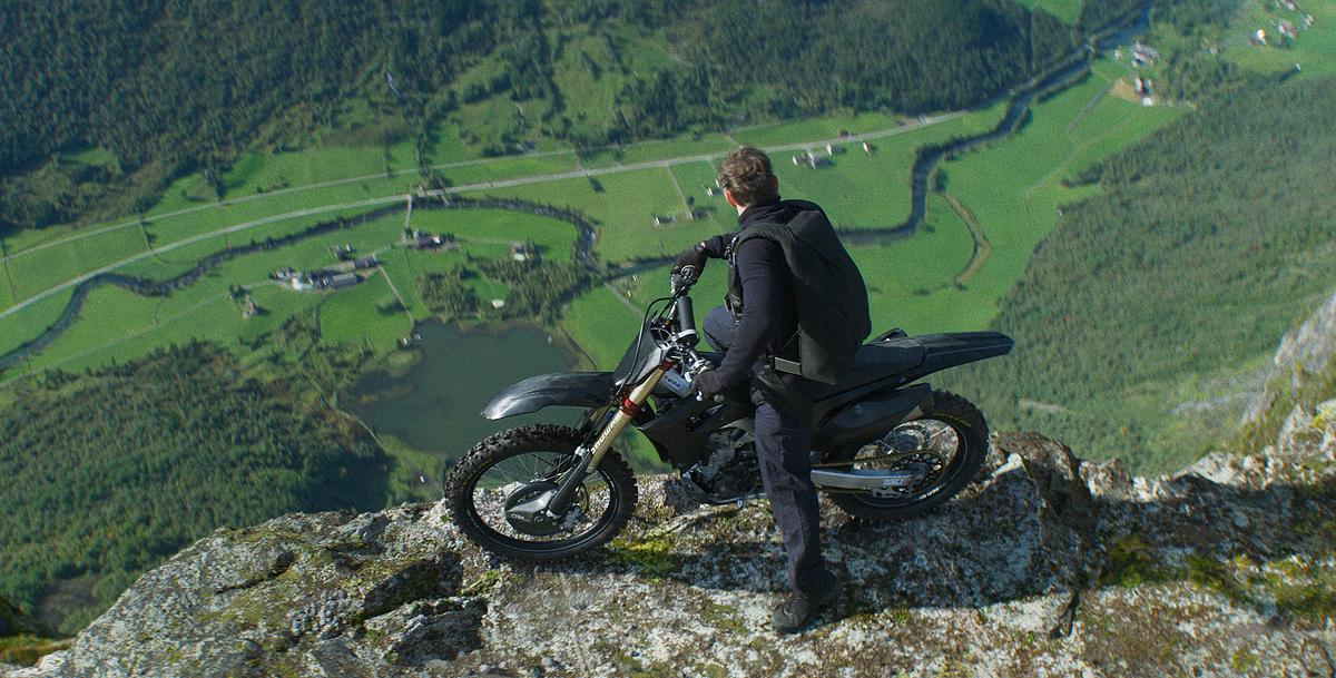 © ORF/PRO7/Paramount Pictures Ein schwarz gekleideter Mann steht mit seinem Motocross-Motorrad knapp an dem Abgrund und blickt ins tiefe grüne Tal