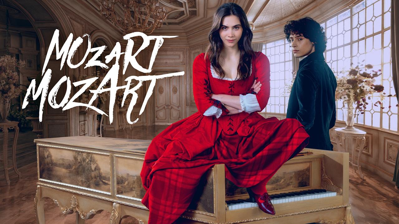 © ORF/WDR/Story House Pictures Maria Anna Mozart in rotem Kleid sitzt auf einem Cembalo, neben ihr steht Wolfgang Amadeus in dunkelblauer Kleidung, in einem prunkvollen Saal - Bildaufschrift MOZART MOZART