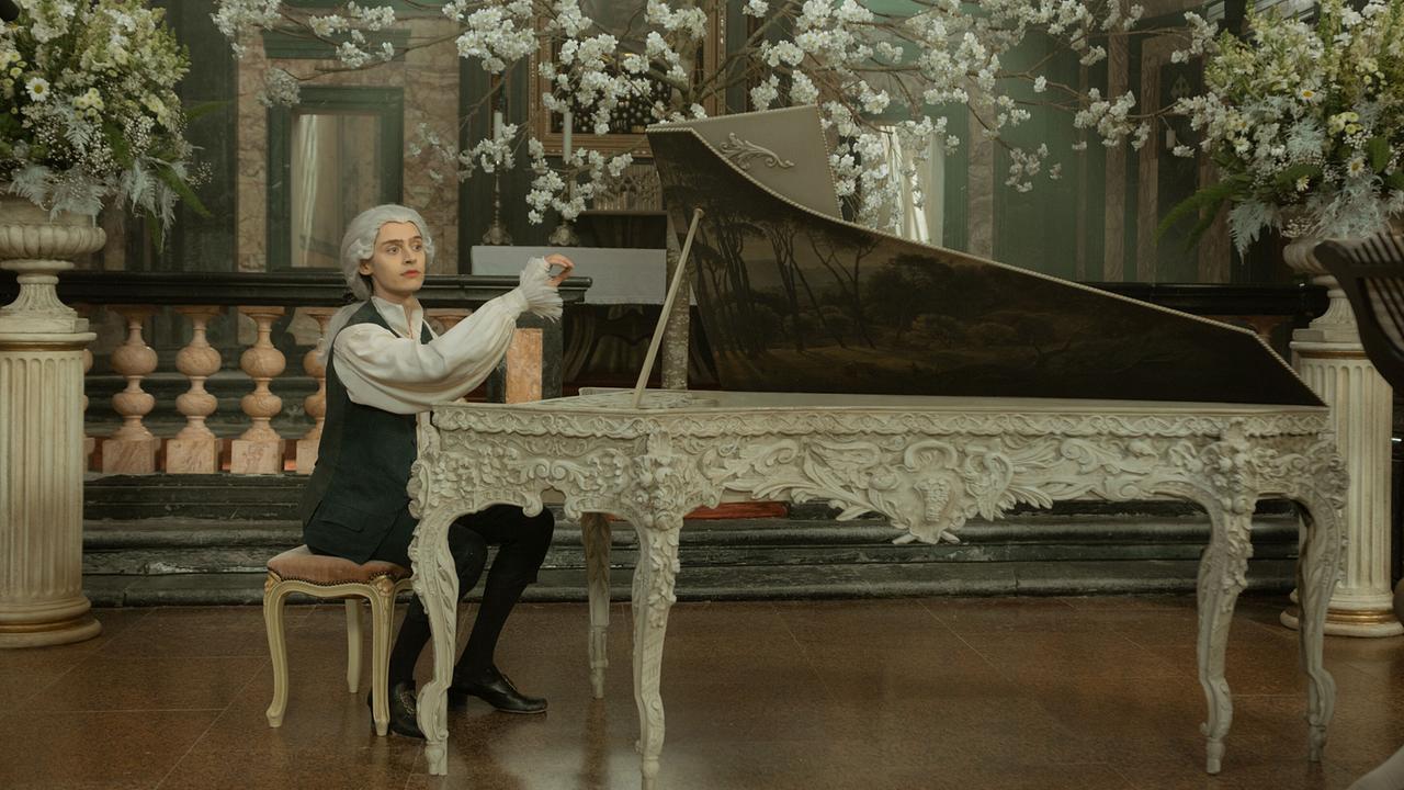 © ORF/WDR/Story House Pictures/Armands Virbulis Wolfgang Amadeus Mozarrt sitzt in historischer Kleidung an einem reich verzierten Cembalo in einem mit Blumen prunkvoll geschmückten Saal