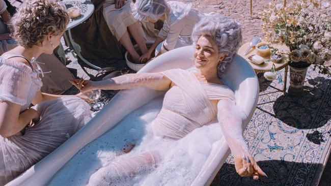Verena Altenberger genießt als Marie Antoinette mit weiß gepuderter Hochfrisur ein Schaumbad im sonnigen Freien und lächelt Gräfin von Greiner an