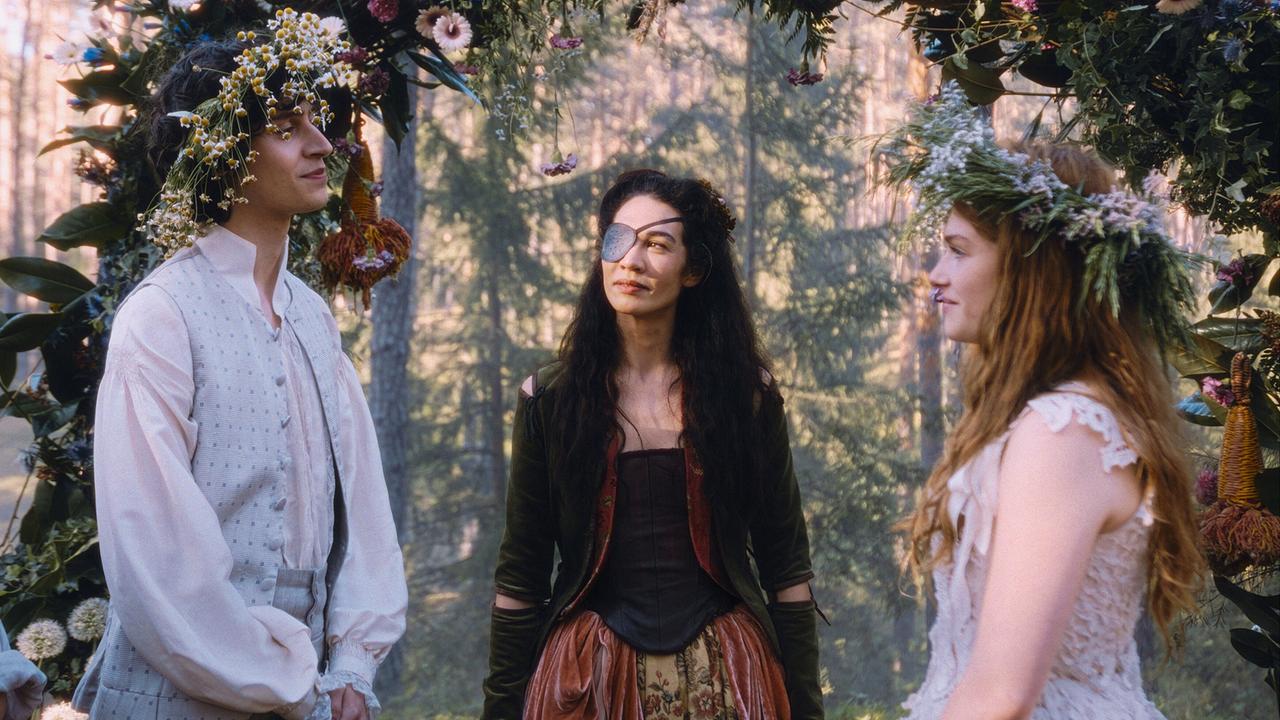 Wolfgang Amadeus und Constanze stehen sich mit Blumenkränzen am Kopf gegenüber, unter einem blumenreichen Torbogen im Wald steht Rosa zwischen den beiden