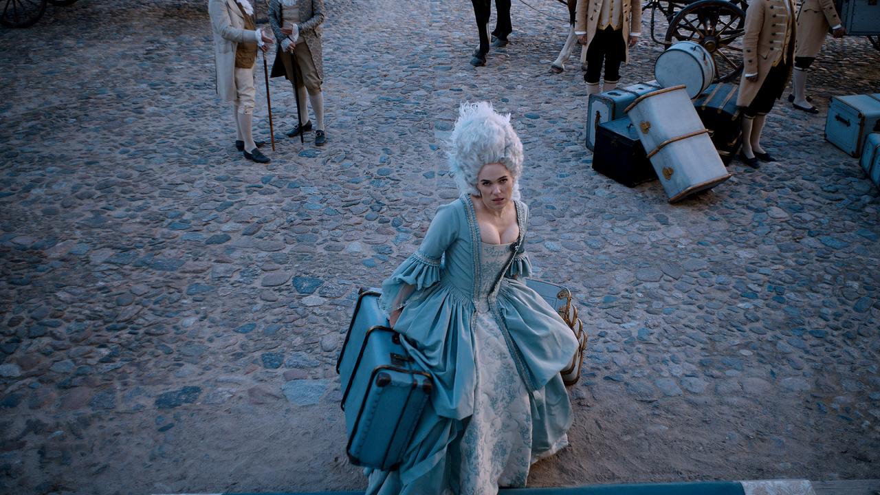 Verena Altenberger als Marie Antoinette im hellblauen Kleid und weißer Hochfrisur, fest entschlossen trägt sie ihre Koffer ins Schloss zurück