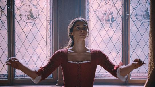 Maria Anna Mozart steht im roten Kleid am Dirigentenpult, sie steht vor großen historisch bemalten Fenstern 