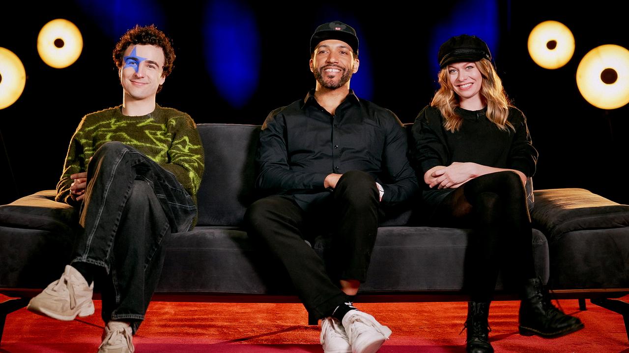 COSMÓ, Cesár Sampson und Zoe Straub sitzen nebeneinander auf einem Sofa in einem Studio mit dunklem Hintergrund und runden Lichtquellen.