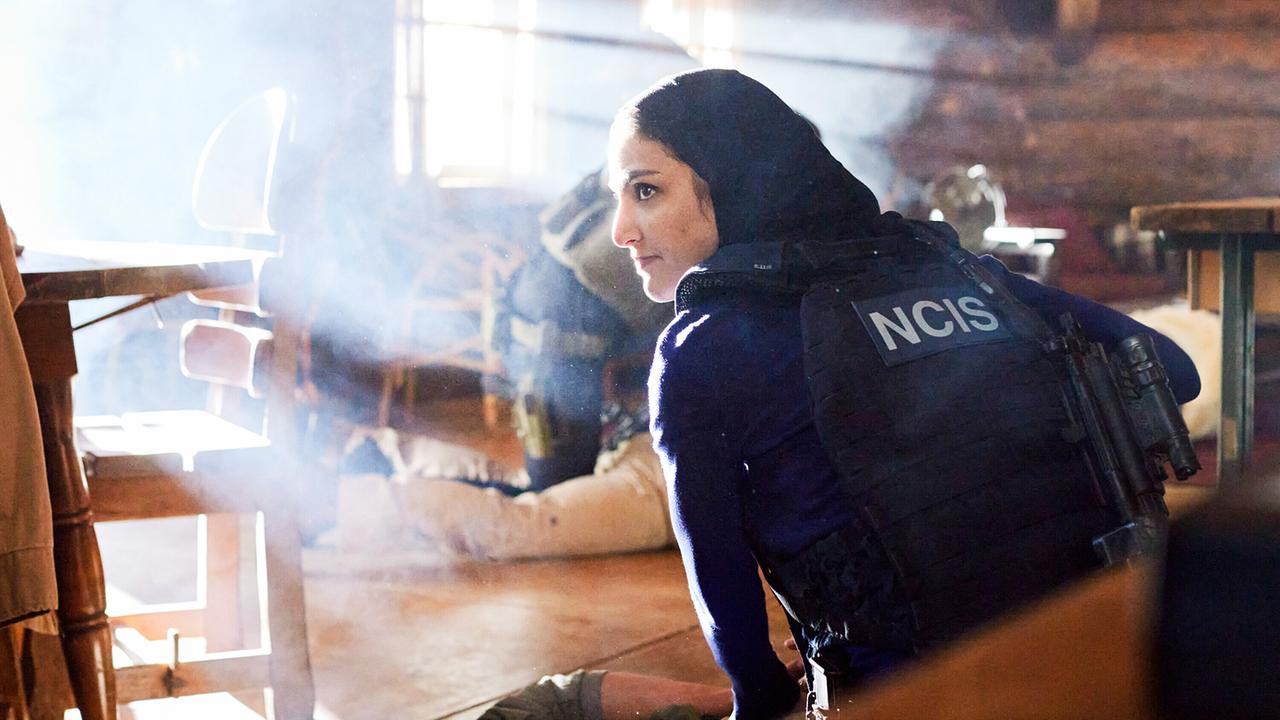 Special Agent Fatima Namazi in taktischer Ausrüstung mit 'NCIS'-Kennzeichnung kniet in einem von Sonnenstrahlen durchfluteten Raum