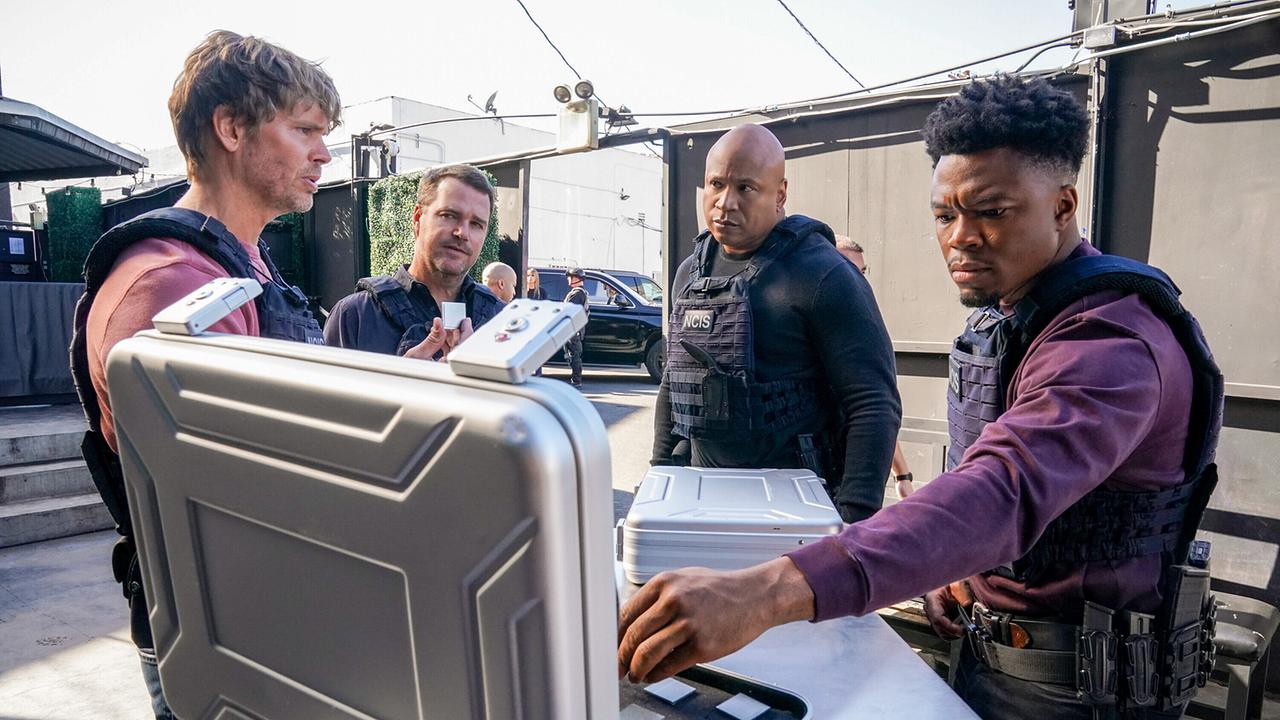 © ORF/Sevenone International/CBS/Sonja Flemming Mehrere Personen in taktischer Ausrüstung stehen im Freien um zwei silberne Koffer, ein Mann nimmt aus dem geöffneten Koffer ein Plättchen