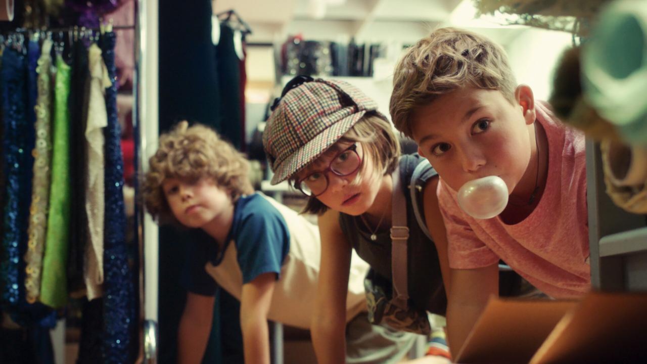 Franz, Gabi und Eberhard schauen krabbelnd zwischen Kleiderständern in einem Geschäft hervor.