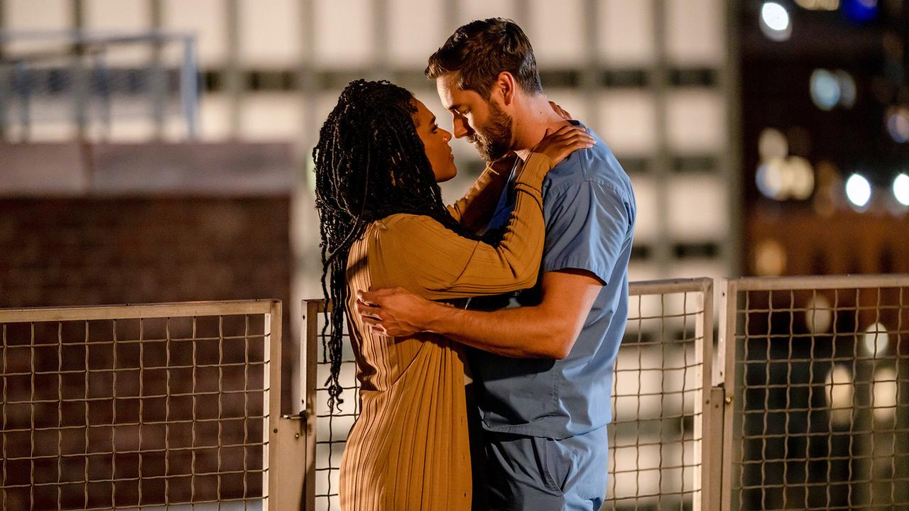 © ORF/Universal/NBC/Zach Dilgard Helen und Max halten sich in den Armen, sie stehen nachts im Freien bei einem Geländer des Krankenhausgebäudes, sie in brauner Strickjacke, er in blauer Ärzte-Bekleidung