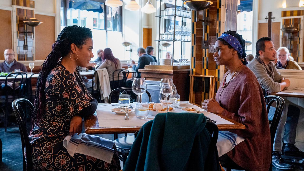 In einem hellen Restaurant sitzen zwei Frauen tagsüber an einem Tisch und unterhalten sich miteinander, der Tisch ist mit Gläsern und Gebäck gedeckt