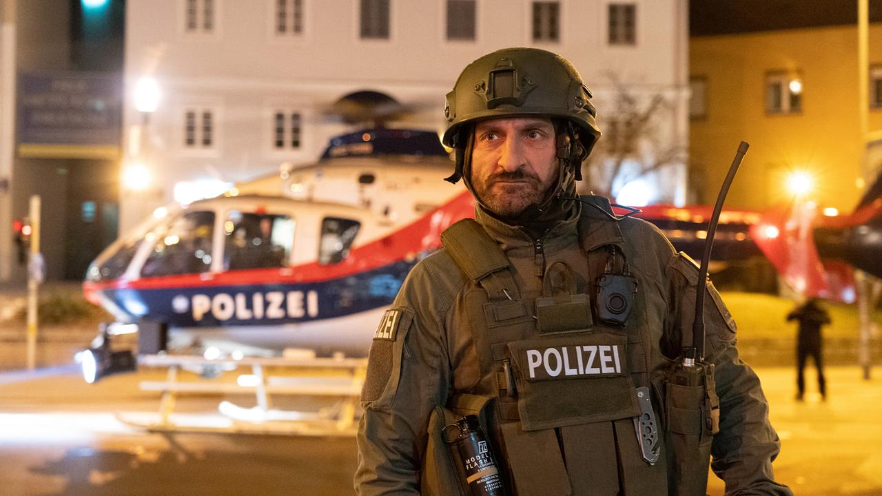 Tim Seyfi in in Polizei-Schutzausrüstung steht nachts an einem Platz vor einem Polizeihubschrauber.