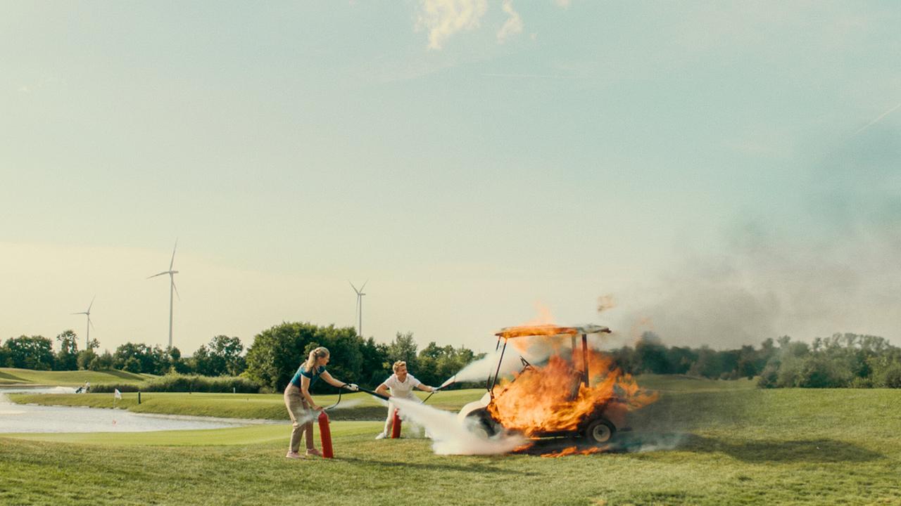 Matthias ist der Mann für alle Fälle und versucht hier mit einer Frau auf einem Golfplatz, einen brennenden Golfwagen mit Feuerlöschern zu löschen.