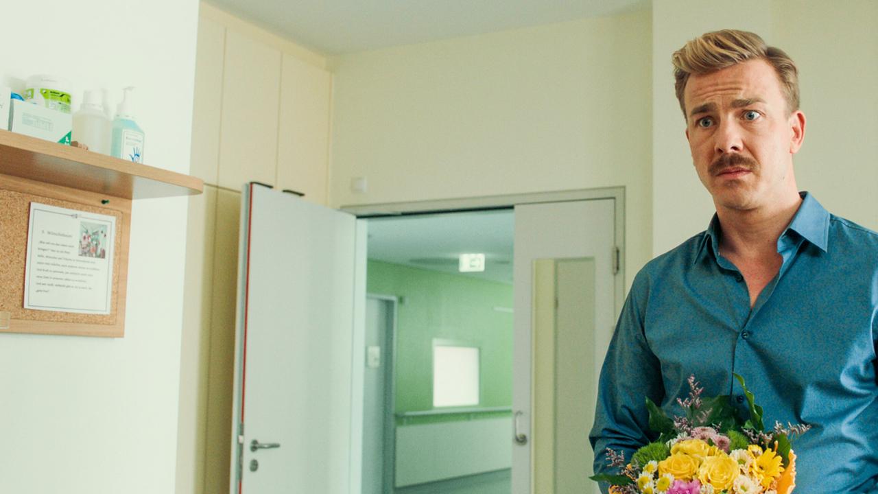 Matthias hält in einem nüchternen Zimmer einen bunten Blumenstrauß.