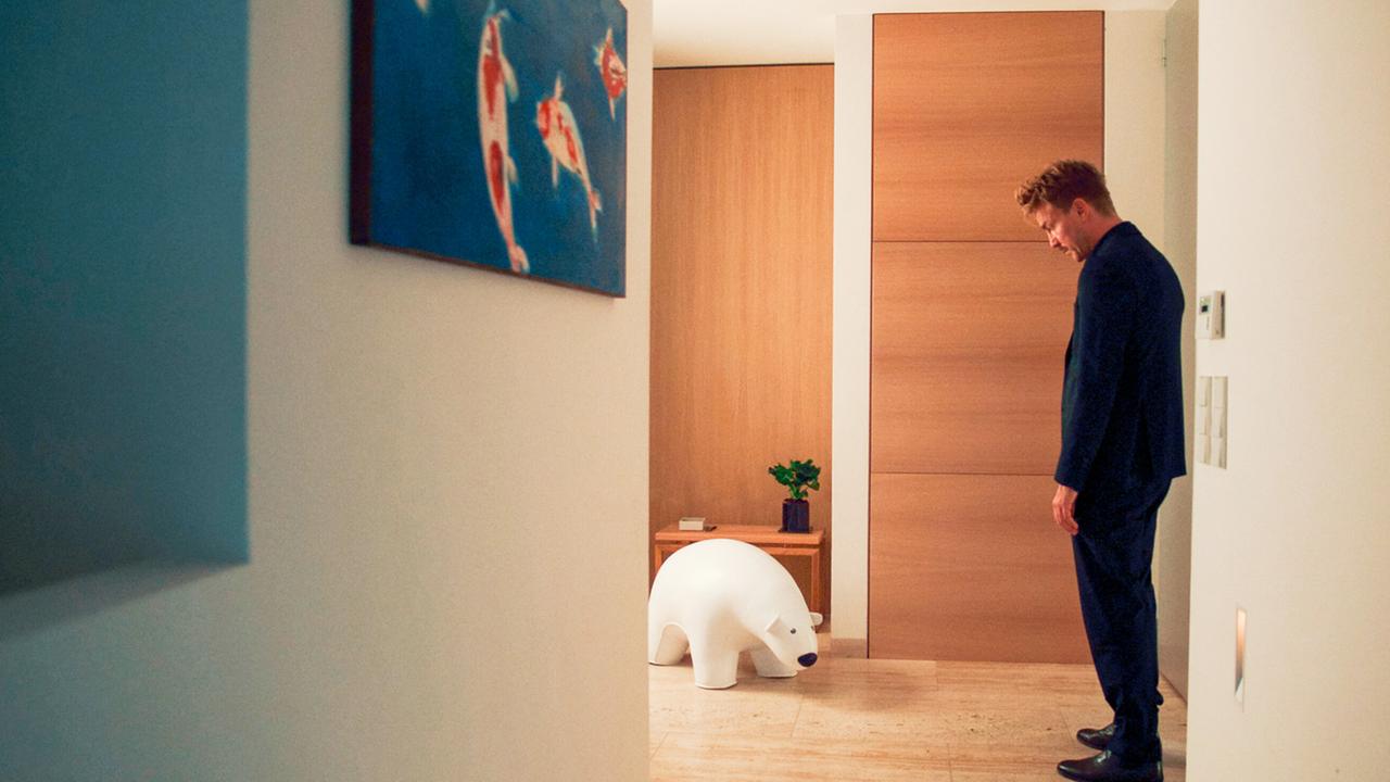 Matthias steht nachdenklich in einem modernen Flur vor einer weißen Eisbärenfigur.