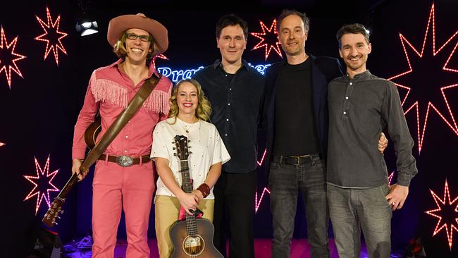 Blonder Engel, Miss Allie, Hosea Ratschiller und Andreas Rainer stehen auf einer Bühne vor bunten Lichtsternen und dem Logo von "Pratersterne - Rote Bar"