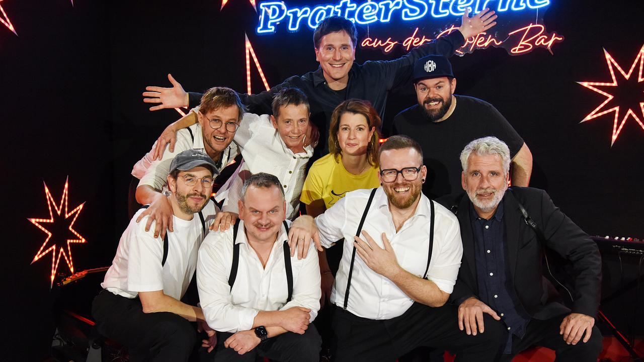 Hosea Ratschiller mit Band 5/8erl in Ehren, Dirk Stermann, Suse Lichtenberger und Michael Bauer stehen auf der Bühne mit leuchtenden Sternen und Neon-Schriftzug "Pratersterne - Rote Bar".