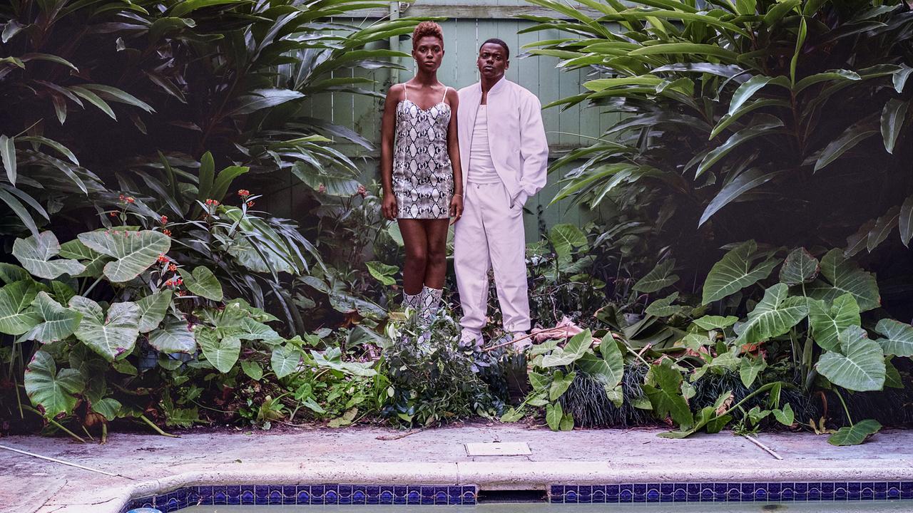 © ORF/Universal Pictures Queen und Slim stehen im Garten vor tropischer Pflanzenkulisse an einem Pool, beide in auffälliger Kleidung – sie im Schlangenmusterkleid, er ganz in Weiß
