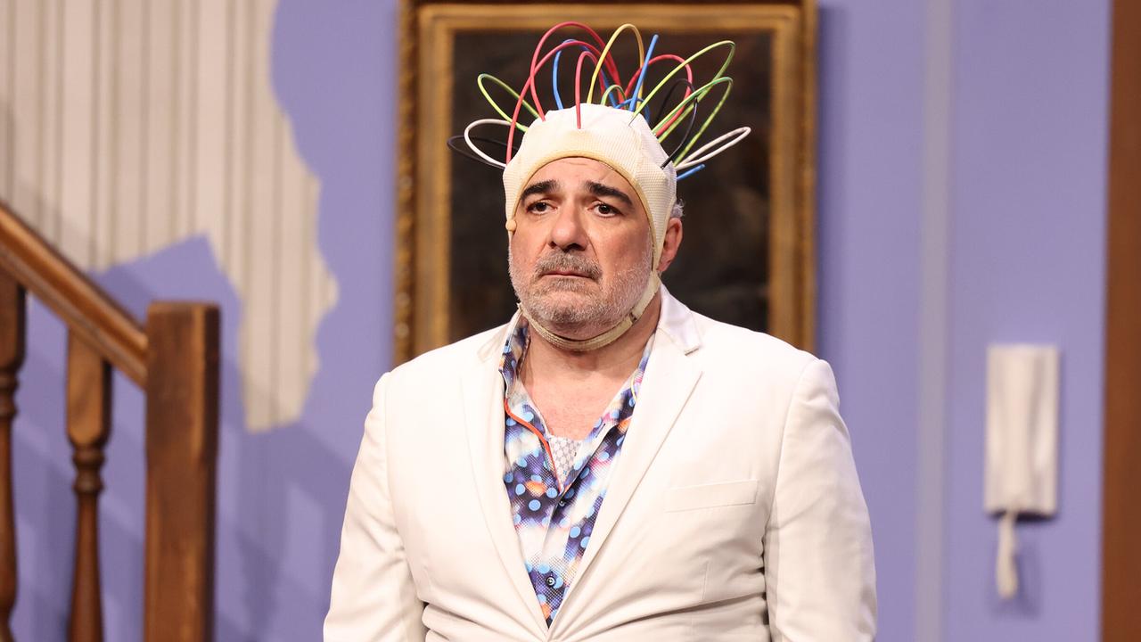 © ORF/Hoanzl/Katharina Schiffl Michael Niavarani im weißen Anzug trägt eine auffällige Kopfbedeckung mit bunten Schläuchen und blickt ernst auf der Bühne von "Reset - Alles auf Anfang".