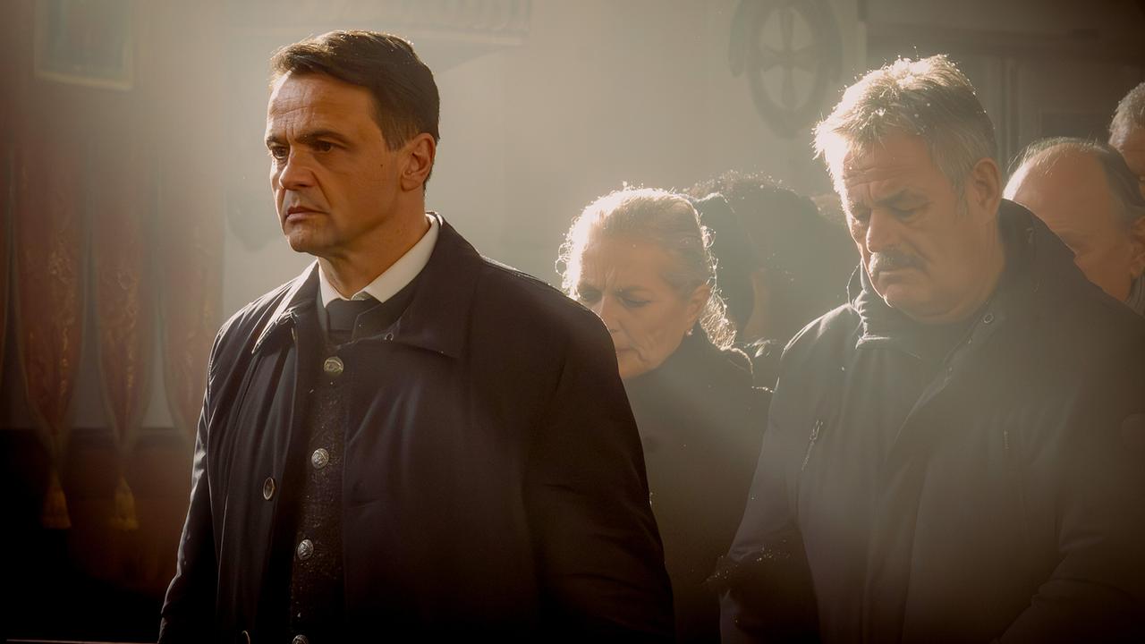 Trauergäste, ihnen voran Bürgermeister Walter, stehen im Lichtkegel in einer Kirche während einer Zeremonie.