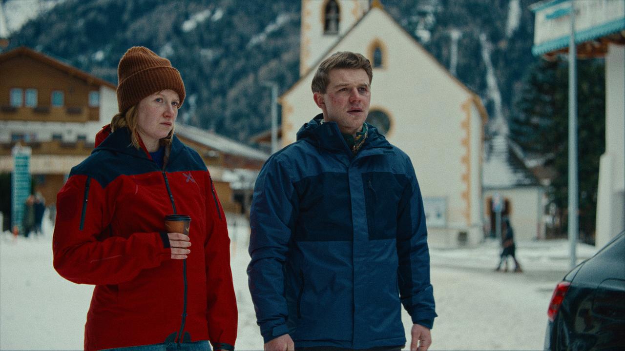 Melanie Grandits, mit einem Becher in der Hand, und Martin Steiner stehen in einem verschneiten Dorf und blicken nach vorne.