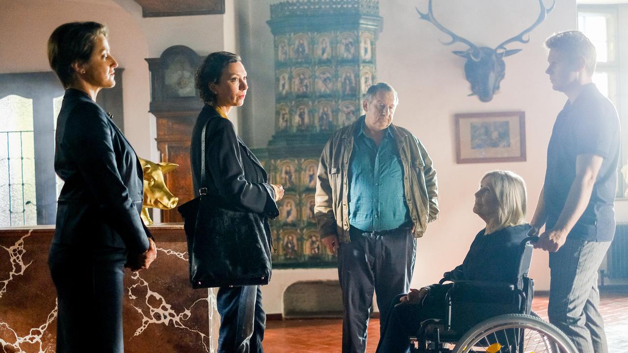 Agathe Mendel, Angelika Schnell, Franitschek, Karoline Dinkelmann im Rollstuhl und Bertram Dinkelmann stehen in einem historischen Raum neben einer goldenen Schweinskulptur auf einem Mamrmorsockel.