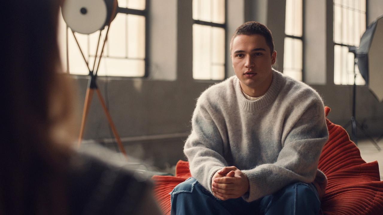 Georg Stoiber sitzt in einem hellen Raum auf einem roten Sofa und führt ein ruhiges Gespräch mit einer ihm gegenübersitzenden Frau.