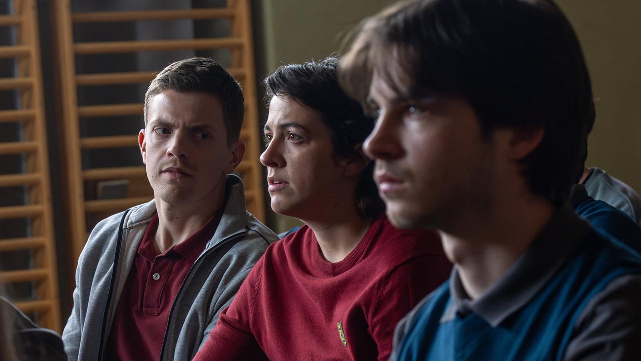 Albin, Tina und Luca Rossi sitzen nebeneinander ernstblickend in einem Turnsaal.