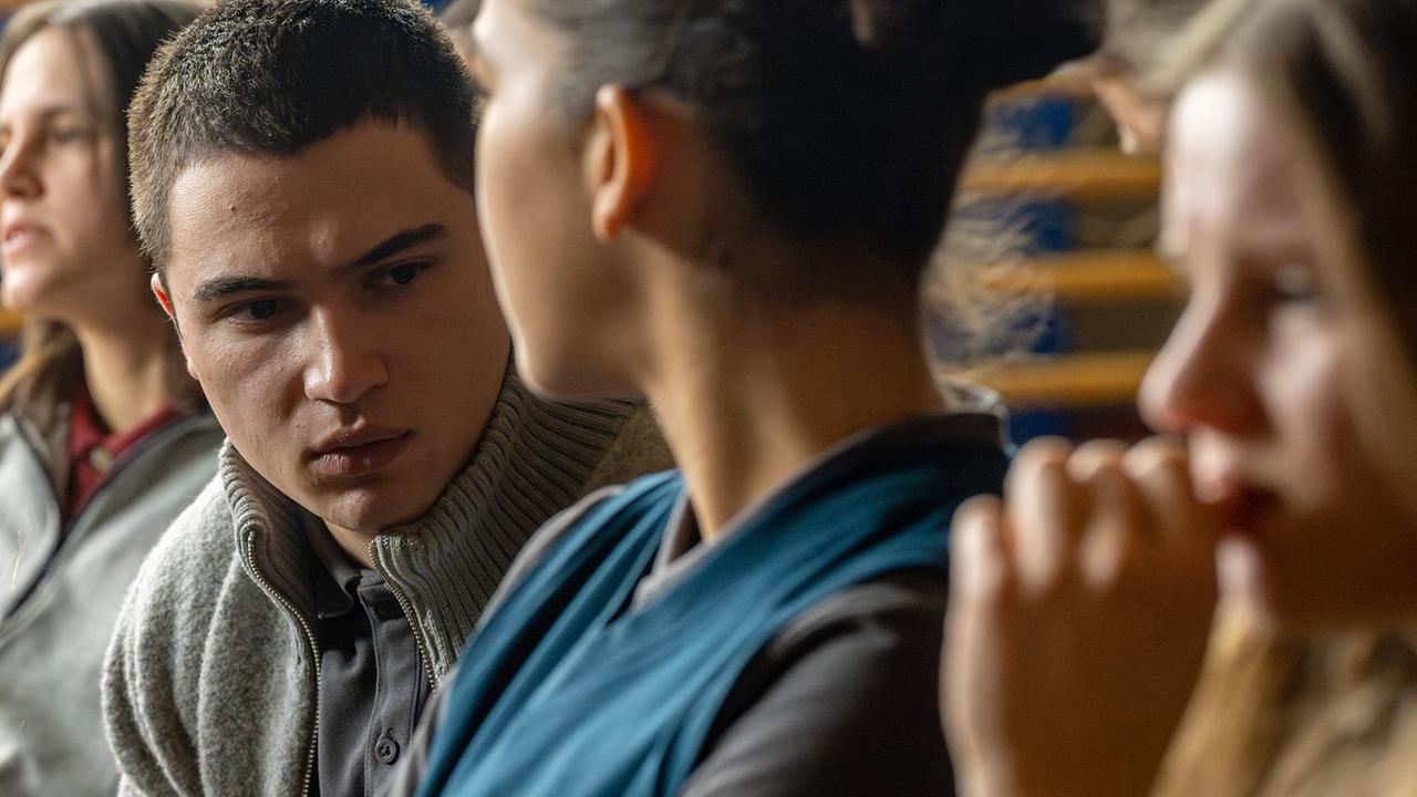 Moritz Uhl, Nawal Ammann und Dani Strobl sitzen nebeneinander in einem Turnsaal und verfolgen etwas.