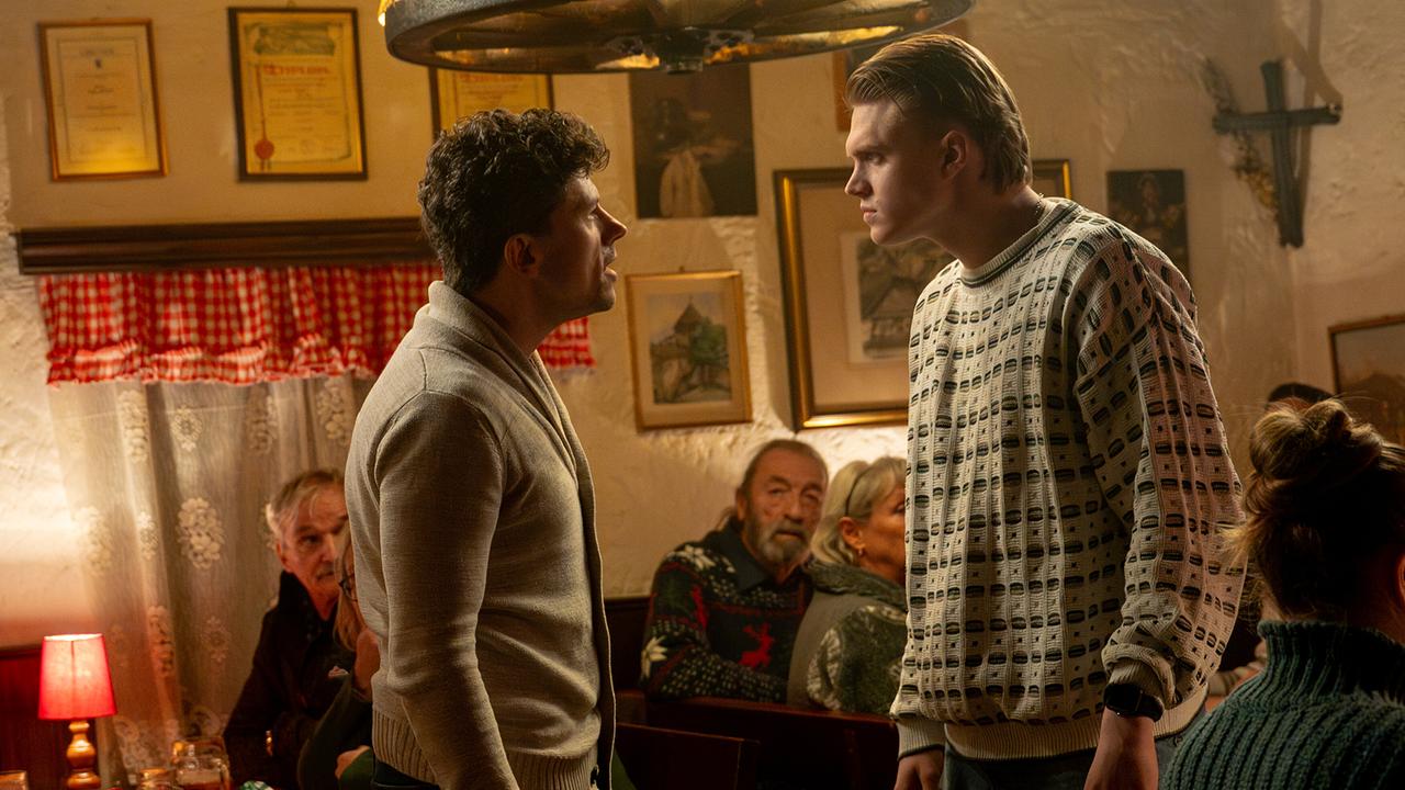 Ein betrunkener Gast und Bobby Harrer stehen sich in einem Gasthaus angespannt gegenüber, im Hintergrund Gäste an den Tischen.