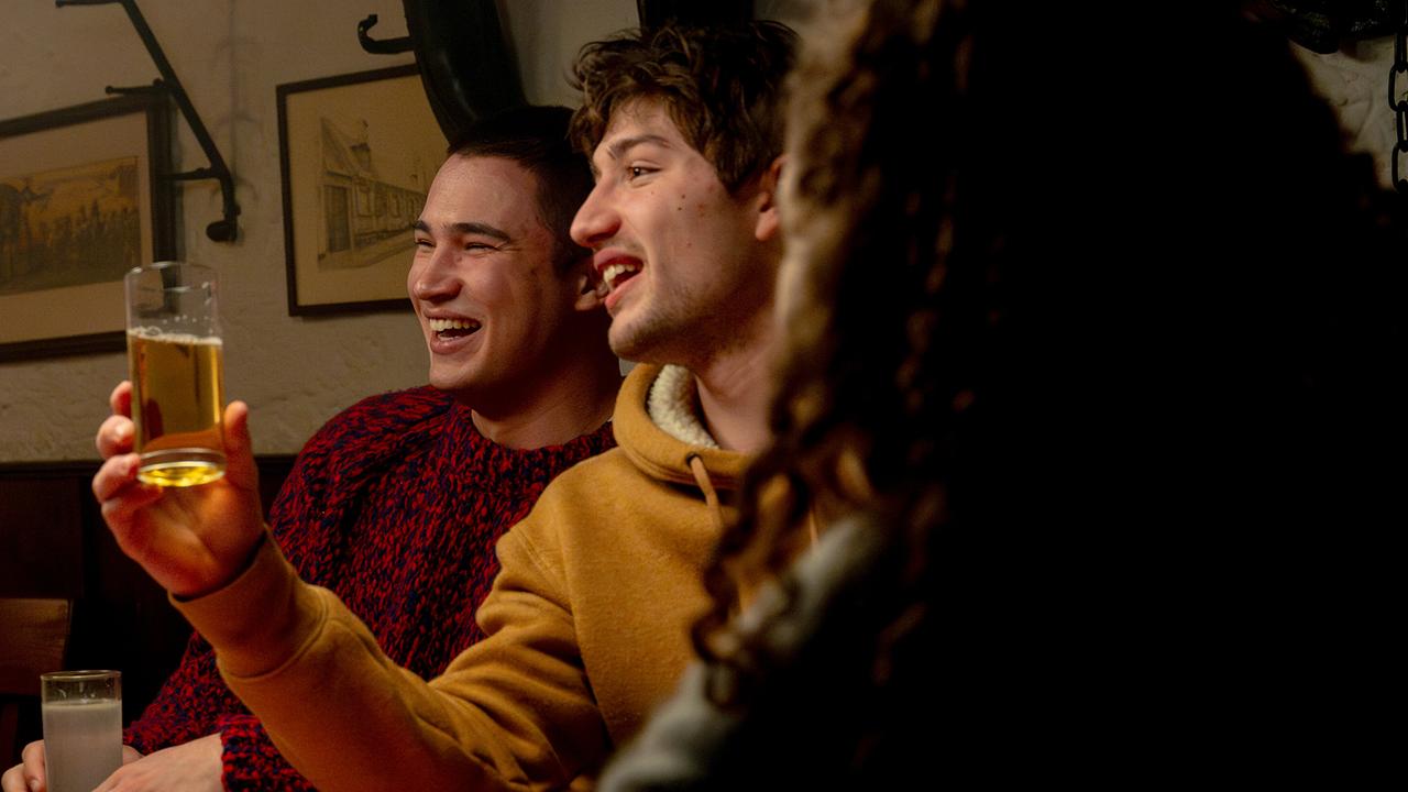 Georg Stoiber, Nikki Auer und Nawal Ammann sitzen gemütlichen in einem Gasthaus, während einer von ihnen ein Glas hebt.