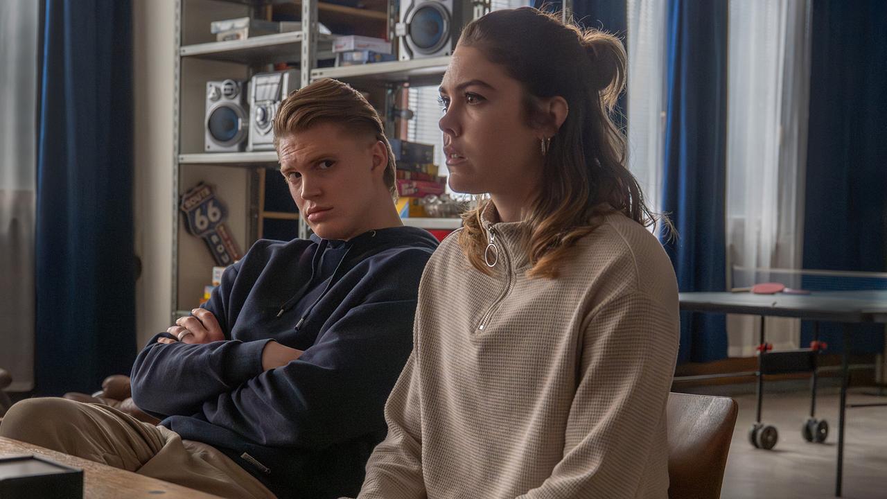 Bobby Harrer sitzt neben Solenn Edenan einem Tisch in einem Aufenthaltsraum.