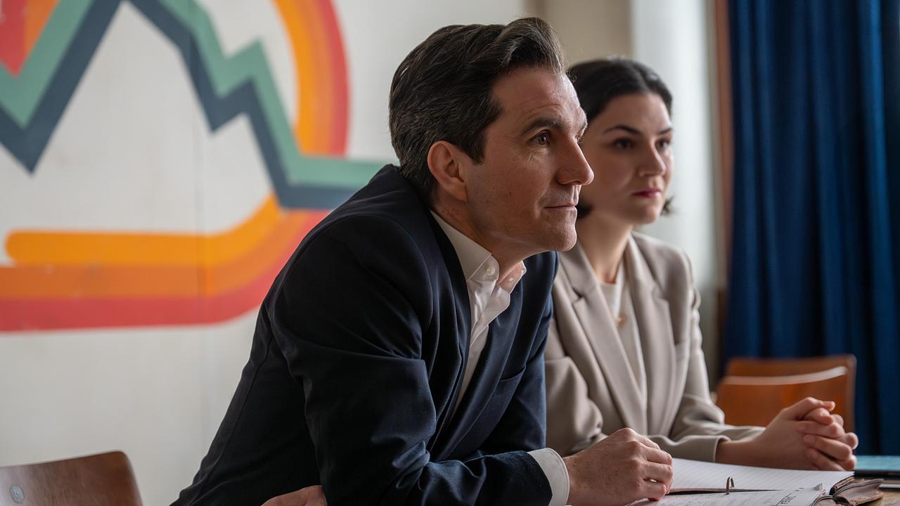 Tony und seine Assistentin sitzen an einem Tisch mit Unterlagen.