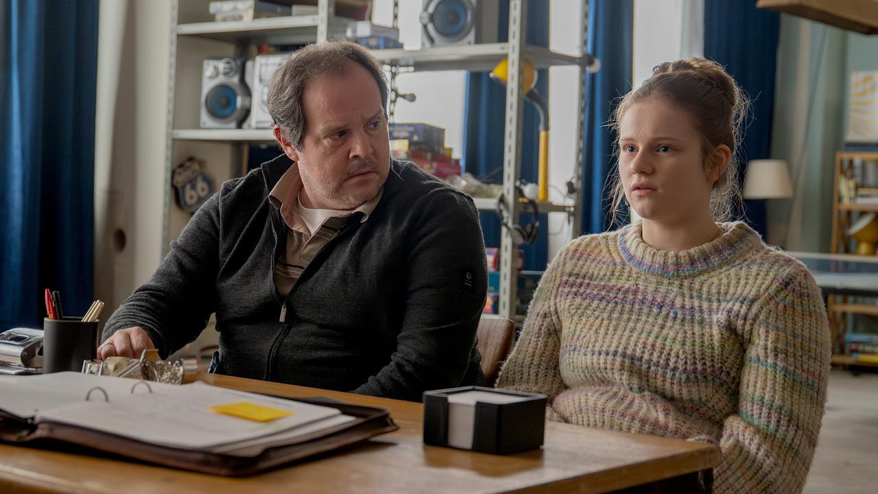 Karl Strobl und Dani Strobl sitzen Seite an Seite an einem Tisch jemandem gegenüber in einem Aufenthaltsraum.