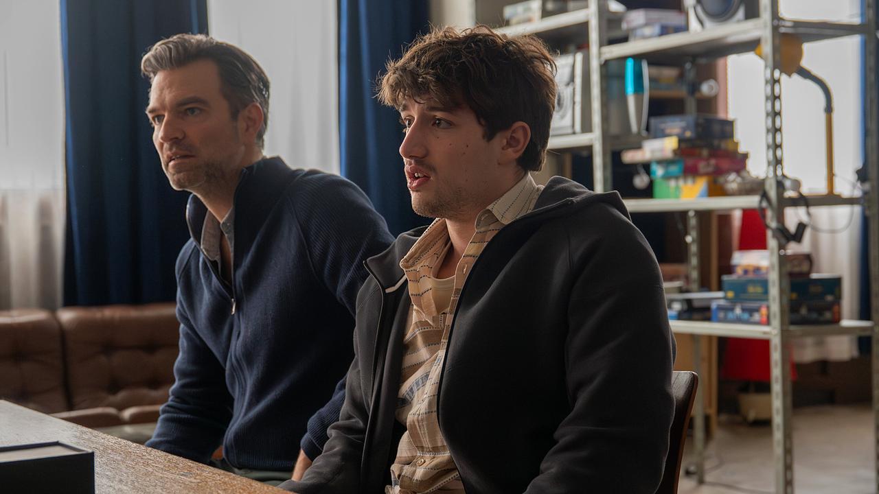 Mark Auer und Nikki Auer sitzen nebeneinander an einem Tisch in einem Aufenthaltsraum und hören jemandem zu.