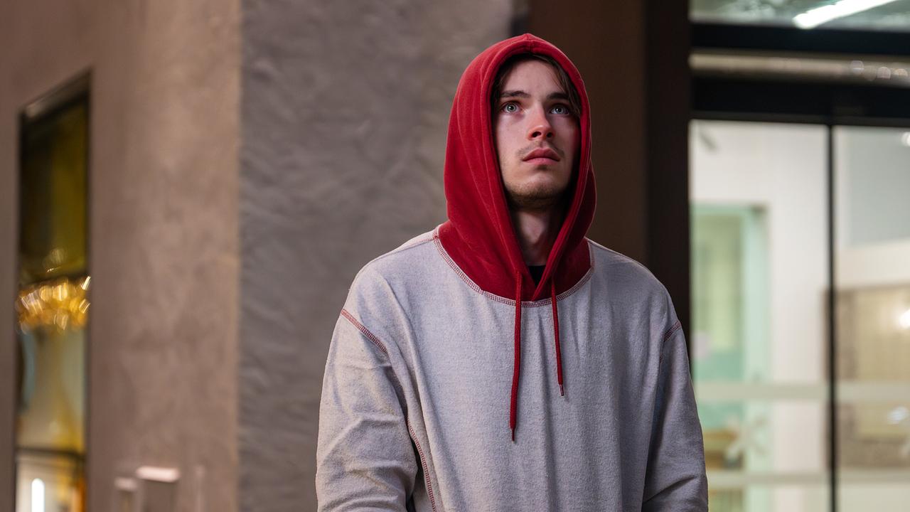 Luca Rossi steht draußen in einer Kapuzenjacke vor einem Gebäude.
